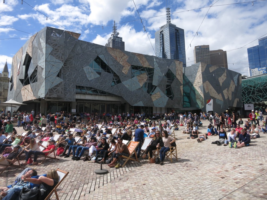 Tennis-Publikum vor futuristischen Bauten am Federation Square